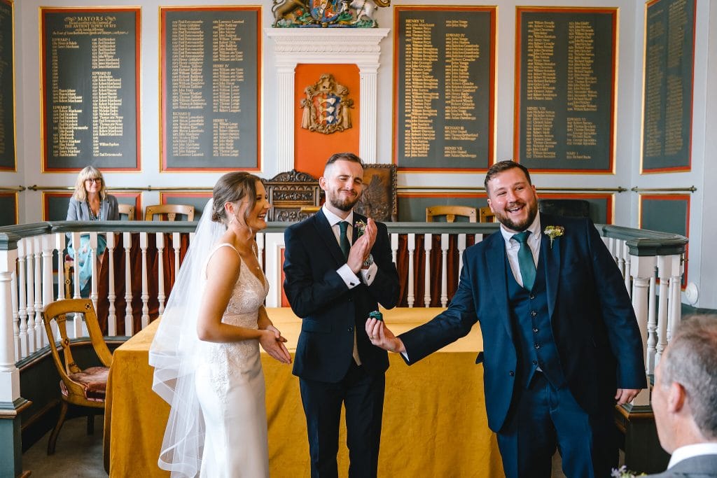Photo from wedding ceremony at Rye Town Hall. The groom applauds the best man as he hands over the wedding rings by Sussex Wedding Photographer, Parkershots